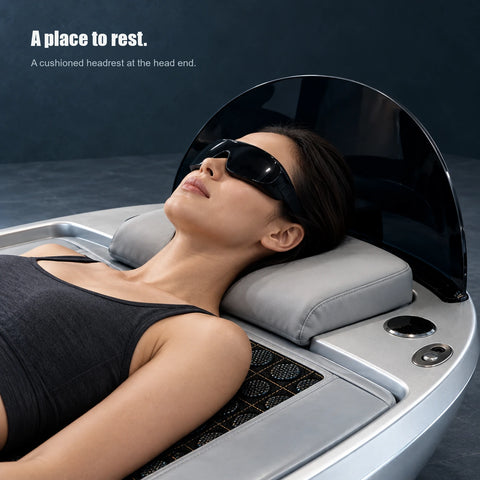 Close view of a woman resting her head on the pale cushion at the capsule head end, wearing opaque black goggles